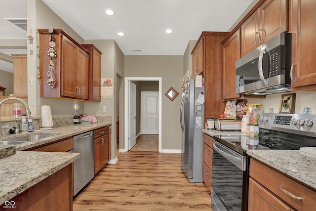 kitchen with light stone counters, a sink, brown cabinets, light wood-style floors, and appliances with stainless steel finishes