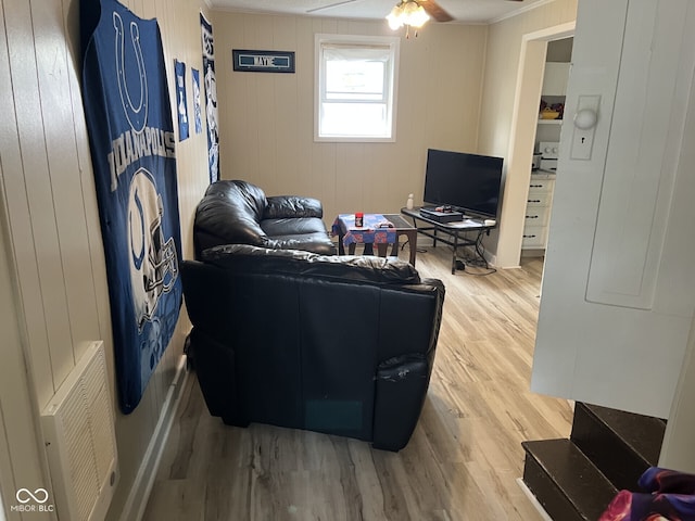 living room featuring wood finished floors, ceiling fan, crown molding, and wooden walls