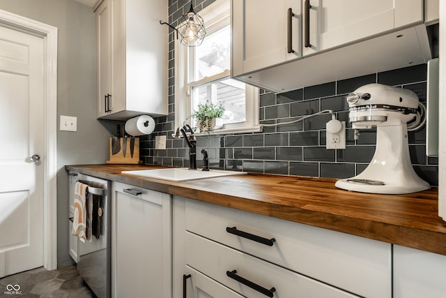 kitchen with wood counters, a sink, tasteful backsplash, dishwasher, and white cabinetry
