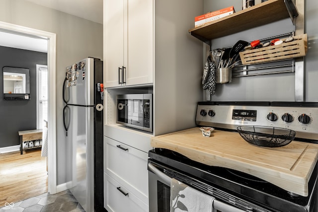 kitchen featuring stainless steel appliances, open shelves, white cabinetry, butcher block counters, and baseboards