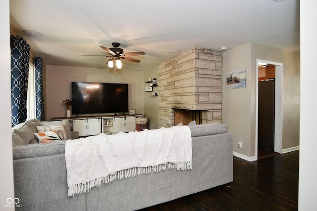 living room featuring a stone fireplace, wood finished floors, baseboards, and ceiling fan