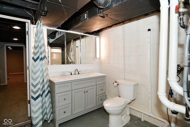 full bath featuring toilet, a shower with curtain, concrete block wall, concrete flooring, and vanity