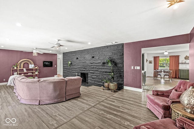 living area with a stone fireplace, wood finished floors, recessed lighting, an accent wall, and baseboards