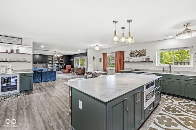 kitchen with wine cooler, a sink, light wood-style flooring, a kitchen island, and healthy amount of natural light