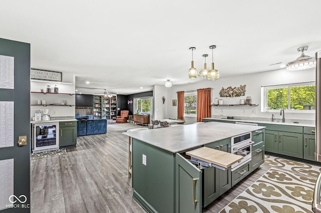 kitchen with green cabinets, wine cooler, a sink, a center island, and light countertops