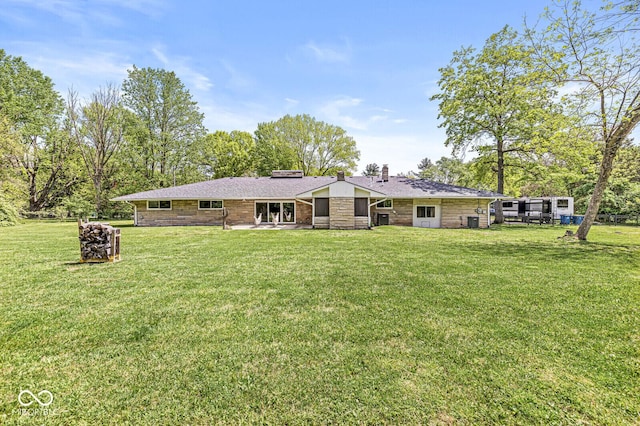 rear view of property with a chimney, a yard, and stone siding