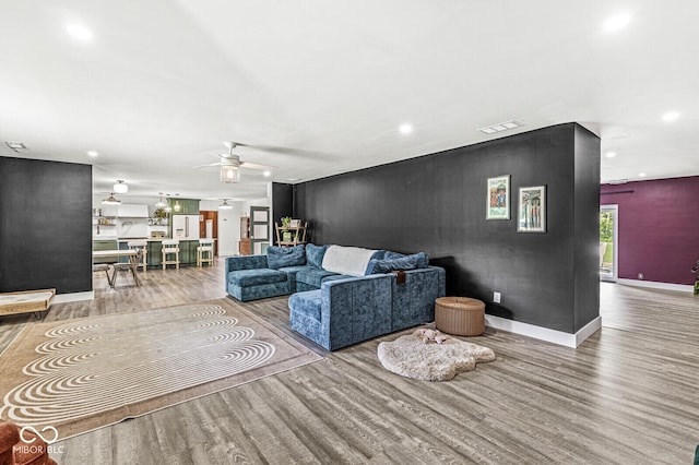 living area featuring wood finished floors, a ceiling fan, recessed lighting, an accent wall, and baseboards