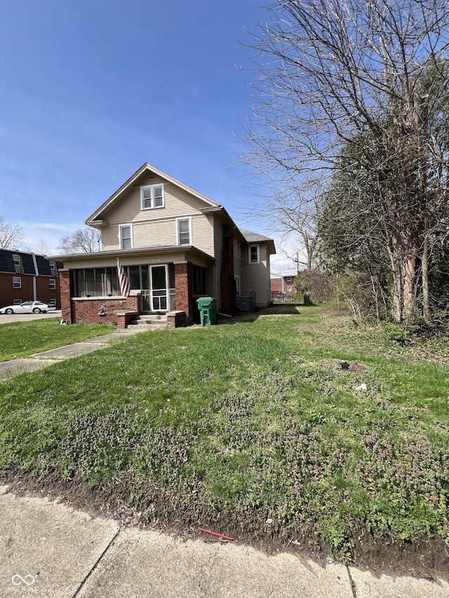 view of front of home with brick siding, a front yard, and central AC unit