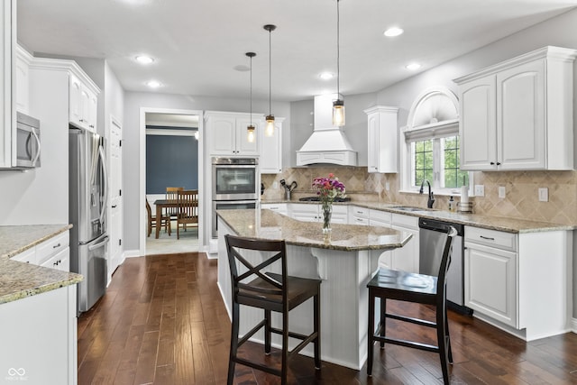 kitchen with custom exhaust hood, appliances with stainless steel finishes, a sink, a breakfast bar, and white cabinetry