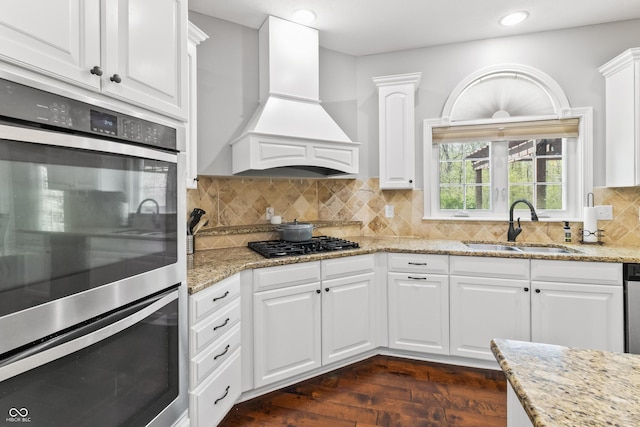 kitchen with premium range hood, a sink, double oven, white cabinetry, and black gas stovetop