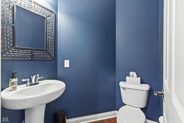 half bathroom with toilet, baseboards, wood finished floors, and a sink