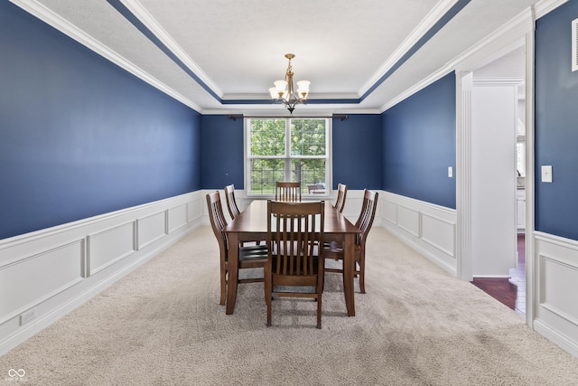 dining room with a decorative wall, a tray ceiling, carpet, a chandelier, and wainscoting