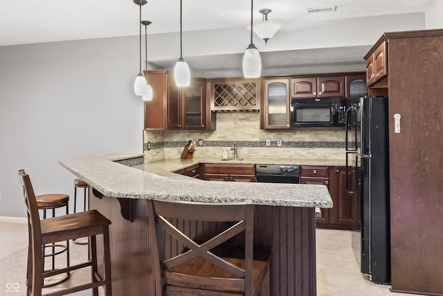 kitchen with black appliances, a peninsula, tasteful backsplash, glass insert cabinets, and a breakfast bar
