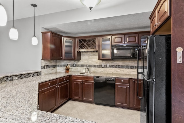 kitchen featuring black appliances, light stone counters, a sink, glass insert cabinets, and decorative backsplash