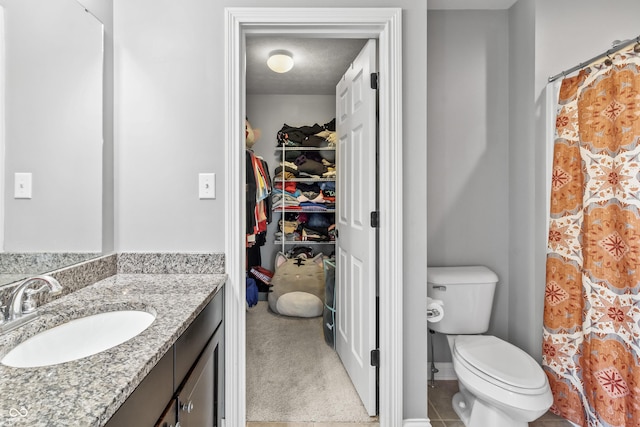 bathroom with toilet, vanity, and a walk in closet