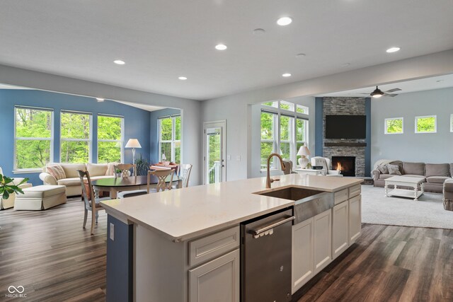 kitchen with open floor plan, a sink, stainless steel dishwasher, a fireplace, and dark wood-style floors