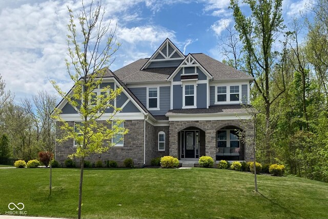 craftsman inspired home with covered porch, stone siding, a front lawn, and a shingled roof