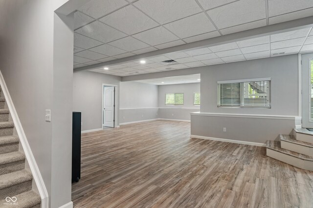 unfurnished room featuring stairs, wood finished floors, baseboards, and a drop ceiling