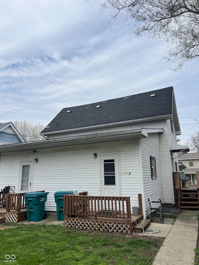 rear view of house featuring a deck, a yard, and roof with shingles