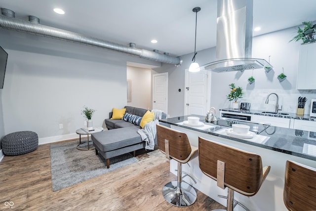 1112 Spann Ave, Indianapolis, IN 46203 - kitchen with island exhaust hood, a sink, wood finished floors, dark stone counters, and a breakfast bar