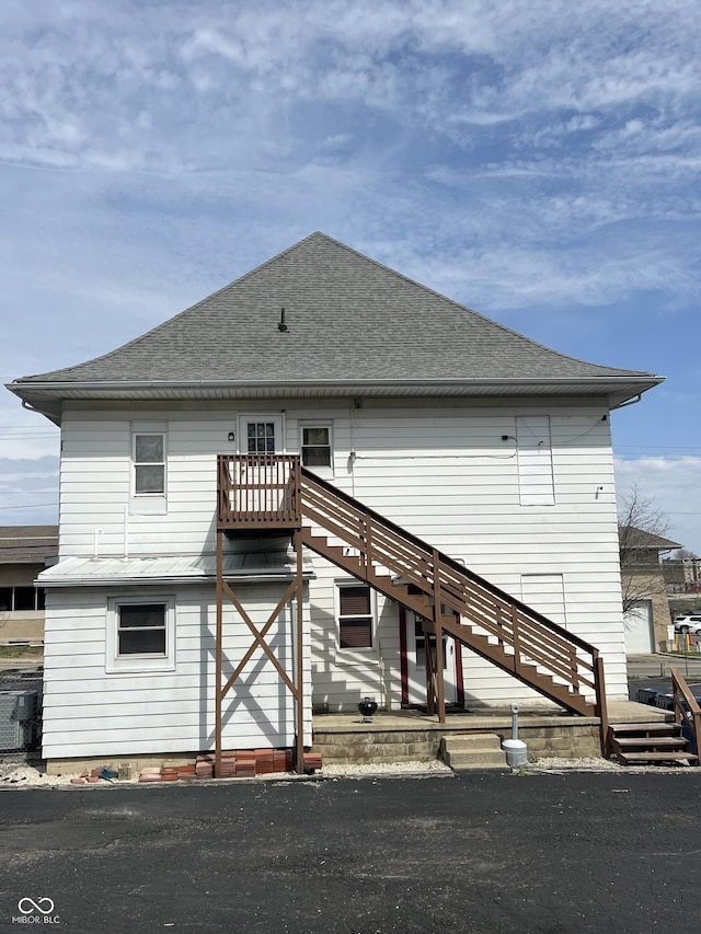 rear view of property featuring stairs and roof with shingles