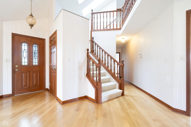 foyer entrance featuring a high ceiling, stairway, light wood-style floors, and baseboards