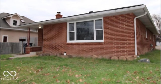 view of home's exterior featuring fence, a chimney, brick siding, and a lawn