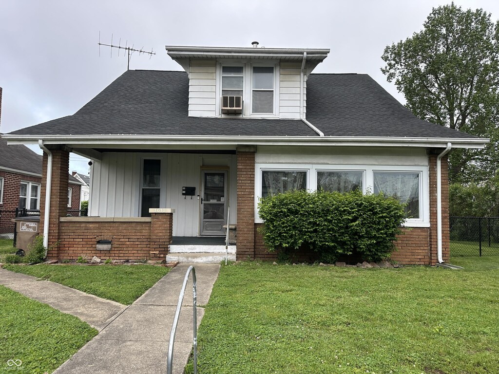 bungalow-style house featuring brick siding, fence, covered porch, a front yard, and roof with shingles