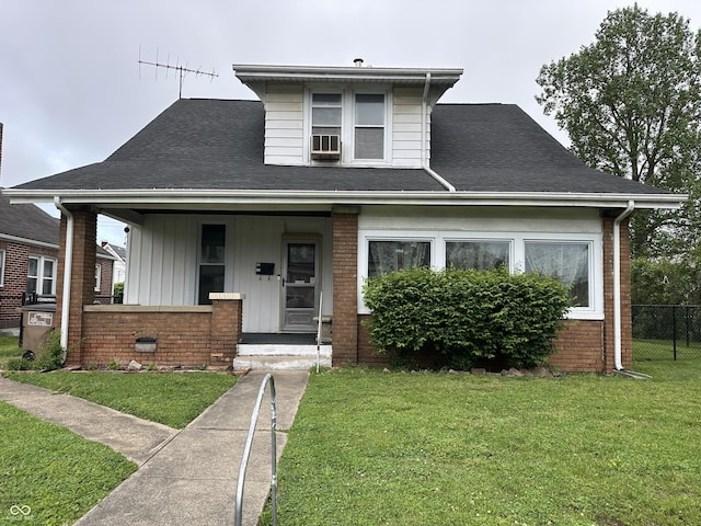 bungalow-style house featuring brick siding, fence, covered porch, a front yard, and roof with shingles