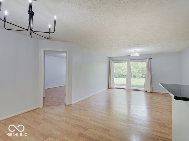 unfurnished living room with a textured ceiling, a chandelier, light wood finished floors, and baseboards