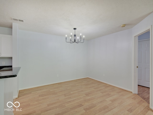 unfurnished dining area featuring light wood finished floors, a chandelier, a textured ceiling, and baseboards