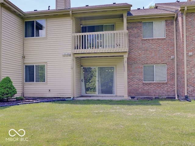 back of house with a balcony, a yard, and brick siding