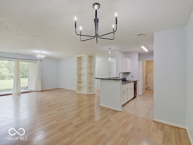 kitchen featuring a chandelier, a textured ceiling, dark countertops, stainless steel dishwasher, and a sink