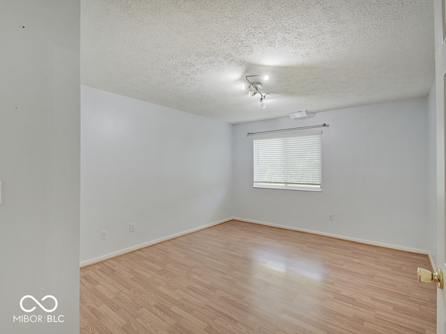 unfurnished room with light wood finished floors, a textured ceiling, and baseboards