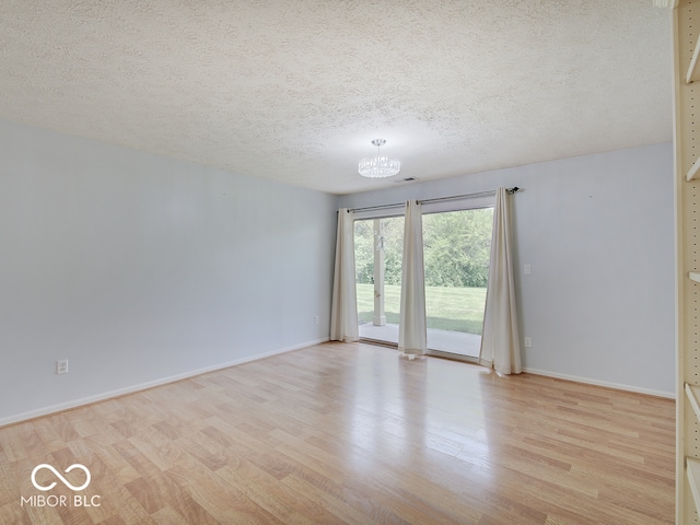 empty room with light wood finished floors, a chandelier, a textured ceiling, and baseboards