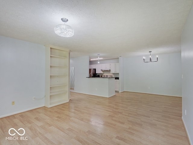 unfurnished living room featuring a chandelier, light wood-style floors, a textured ceiling, and baseboards