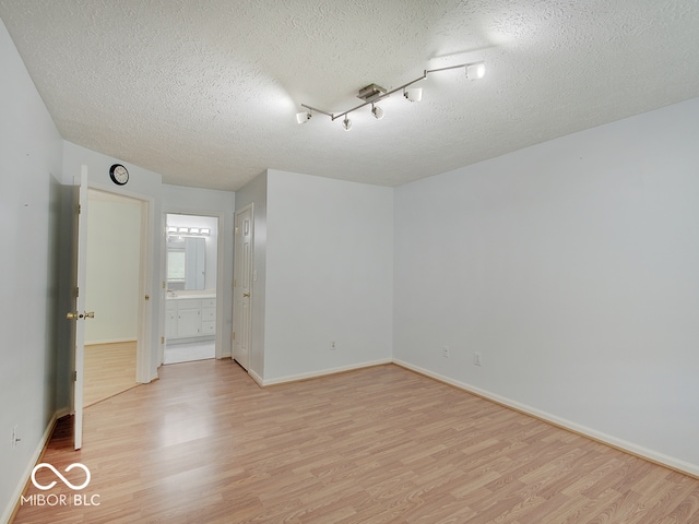 spare room with light wood-style flooring, a textured ceiling, and baseboards