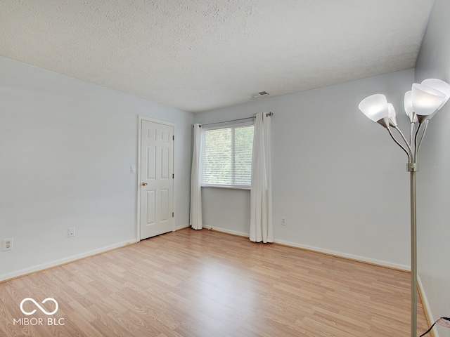 spare room with light wood finished floors, a textured ceiling, and baseboards