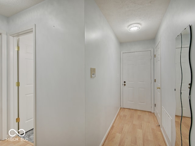 corridor with a textured ceiling, light wood-style floors, and baseboards