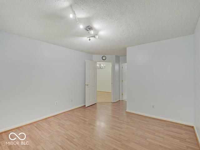 unfurnished room featuring light wood finished floors, a textured ceiling, baseboards, and track lighting