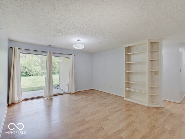 unfurnished room with light wood-type flooring, a textured ceiling, baseboards, and a chandelier