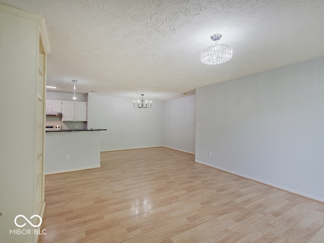 unfurnished living room featuring a chandelier, light wood finished floors, a textured ceiling, and baseboards