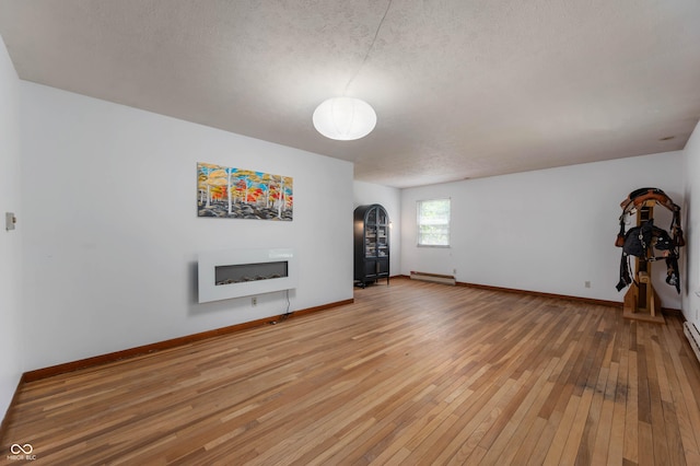 unfurnished living room with arched walkways, baseboard heating, a fireplace, light wood finished floors, and a textured ceiling