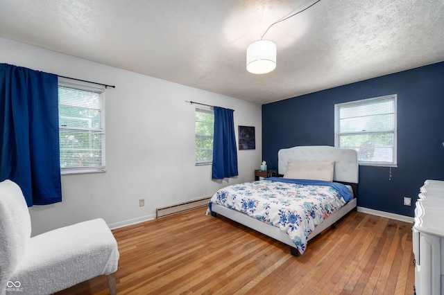bedroom with baseboard heating, hardwood / wood-style floors, and baseboards