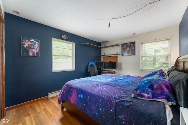 bedroom with hardwood / wood-style floors, a baseboard heating unit, and baseboards