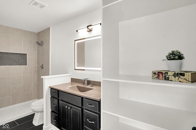 bathroom featuring toilet, tile patterned flooring, vanity, and tiled shower