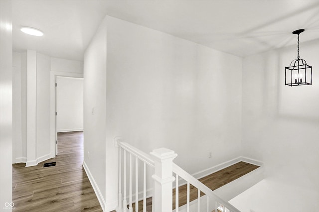 hall with an upstairs landing, wood finished floors, baseboards, and a chandelier