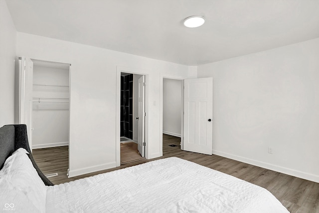 bedroom with wood finished floors, baseboards, a spacious closet, and a closet