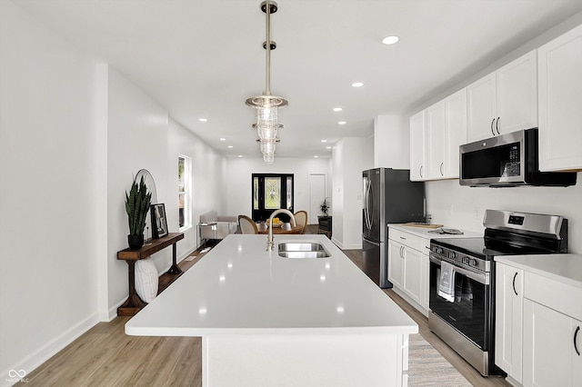 kitchen featuring appliances with stainless steel finishes, a sink, light wood-type flooring, light countertops, and an island with sink