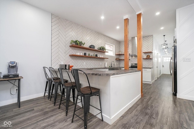 1009 Harrison St, Indianapolis, IN 46202 - kitchen featuring open shelves, dark countertops, wall chimney exhaust hood, a kitchen bar, and a peninsula